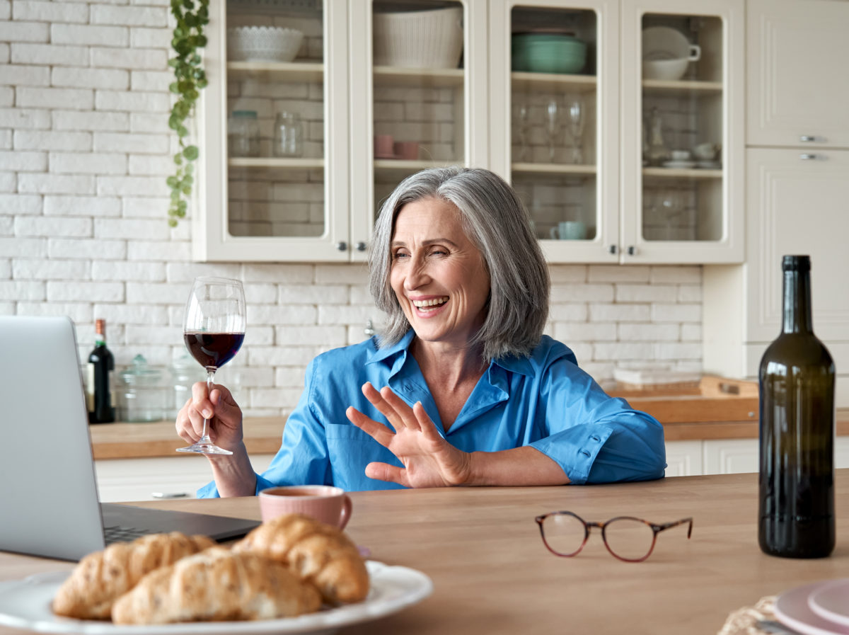 Happy 60s mature woman drinking wine as part of a virtual college class reunion