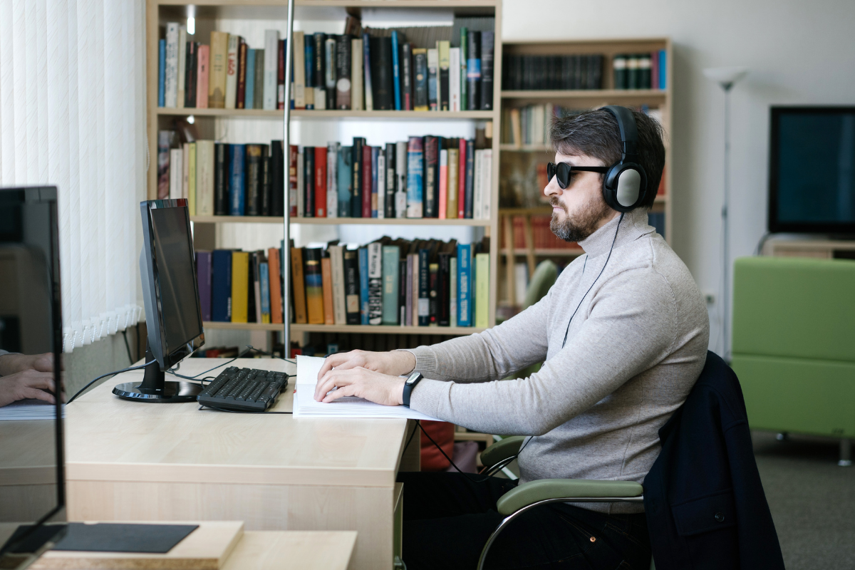 Man wearing headphones and dark glasses, participating in an online meeting on a desktop computer.