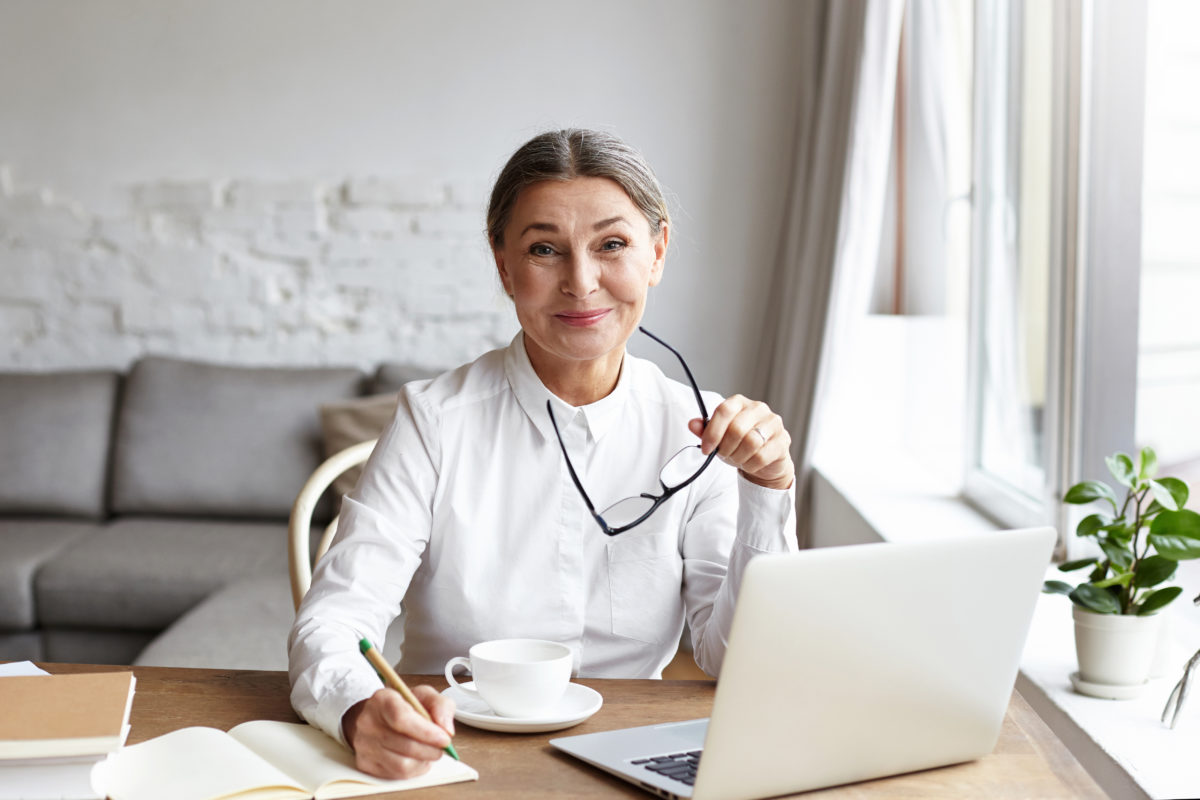 Middle aged woman smiling as she participates in her company's virtual kickoff from her home office